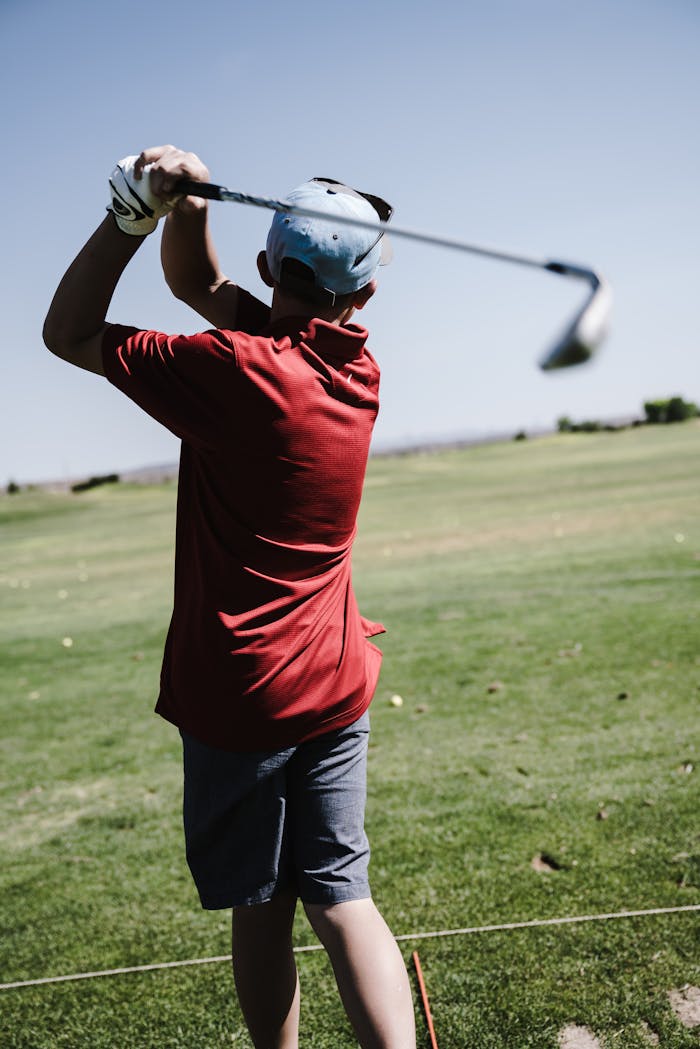 A golfer in a red shirt executes a powerful swing on a sunny golf course.